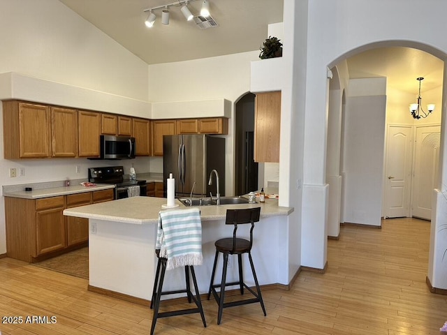 kitchen with appliances with stainless steel finishes, arched walkways, a sink, a peninsula, and high vaulted ceiling