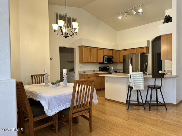 dining room with high vaulted ceiling, a chandelier, arched walkways, track lighting, and light wood-style floors