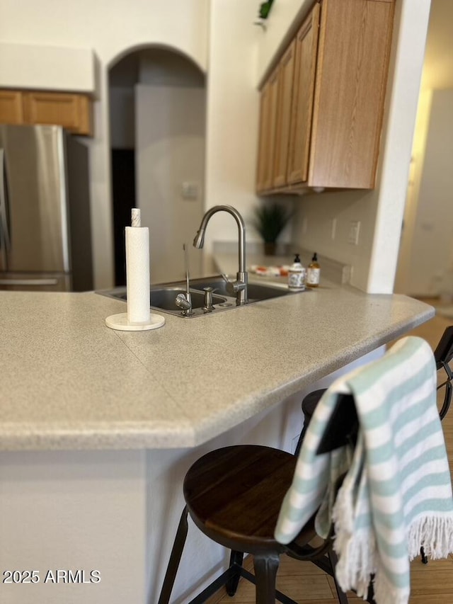 kitchen featuring freestanding refrigerator, a peninsula, brown cabinetry, and a breakfast bar