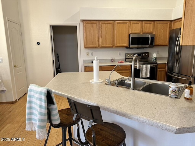 kitchen with stainless steel appliances, a breakfast bar, light wood-style floors, brown cabinetry, and light countertops