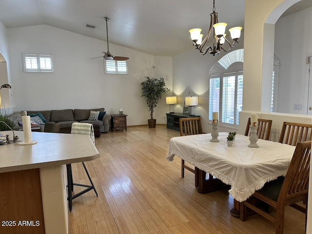 dining room with arched walkways, a ceiling fan, a chandelier, light wood-style floors, and vaulted ceiling