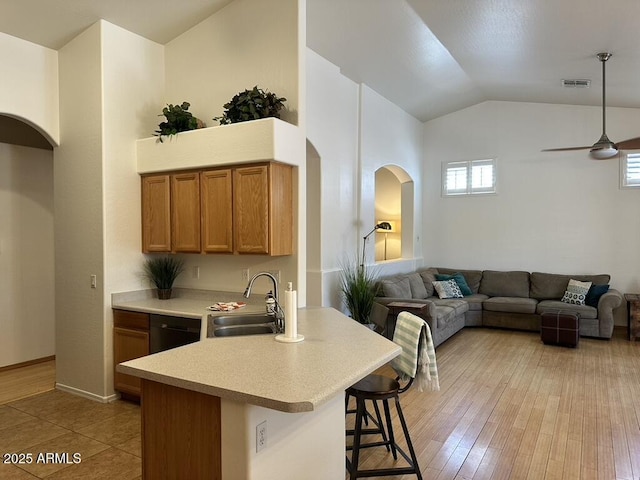 kitchen with a sink, a kitchen bar, light countertops, arched walkways, and brown cabinetry
