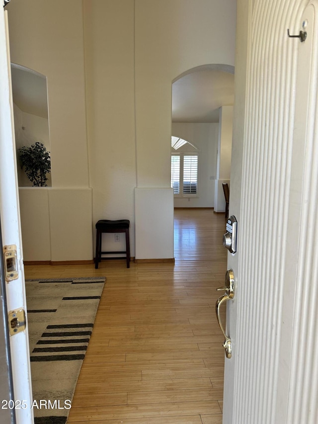 corridor featuring arched walkways and light wood-style flooring
