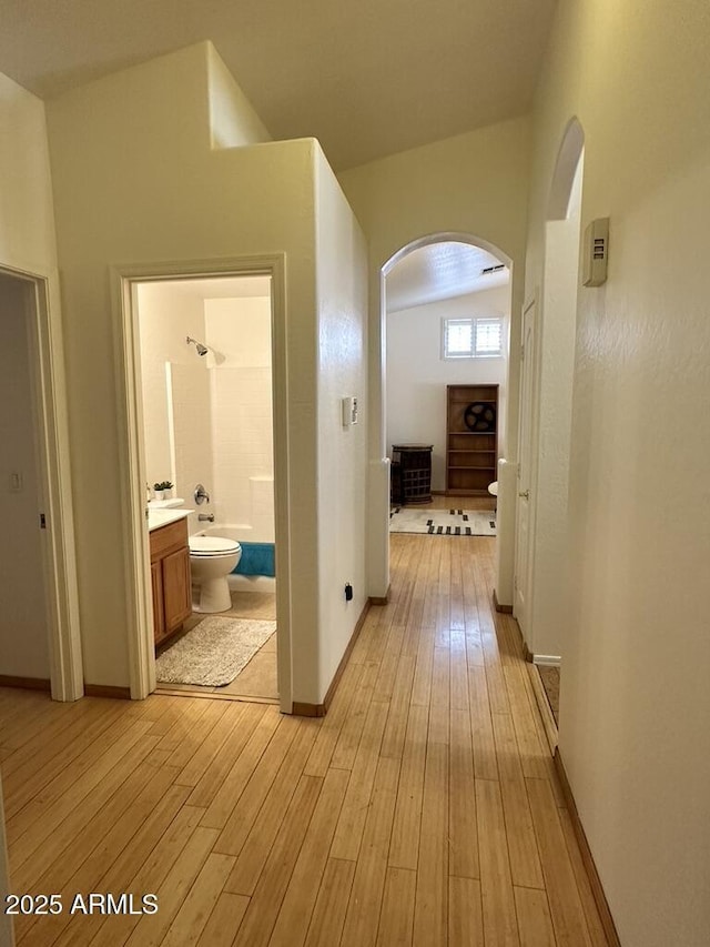 hall featuring arched walkways, light wood-style floors, and baseboards