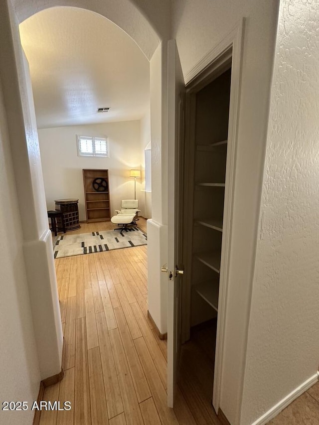 corridor with light wood-type flooring, arched walkways, baseboards, and a textured wall