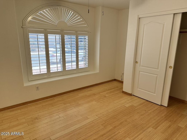unfurnished bedroom with a closet, light wood finished floors, and baseboards