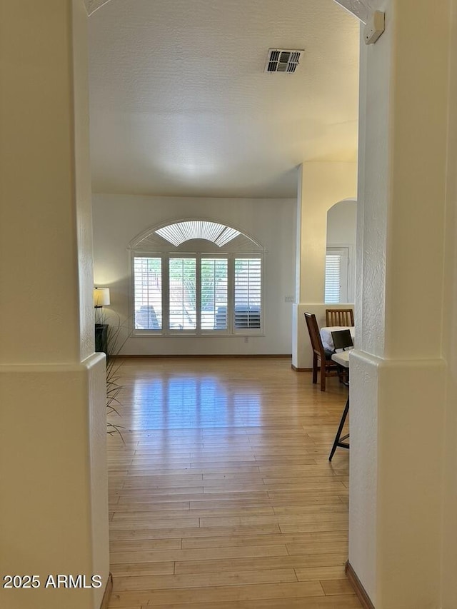 corridor with light wood-style flooring and arched walkways