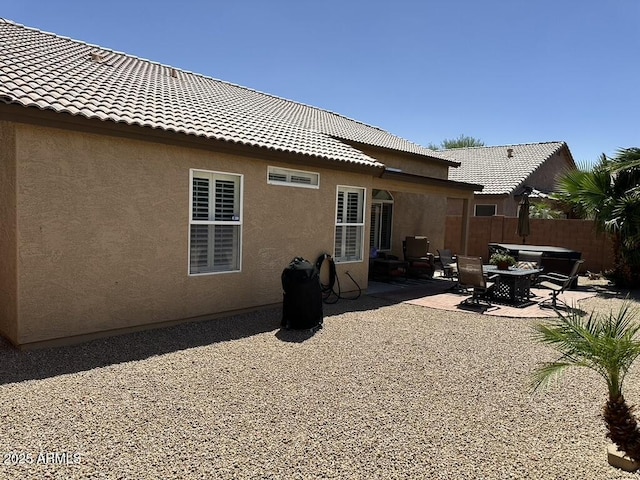 rear view of property with stucco siding, fence, a patio, and a tile roof