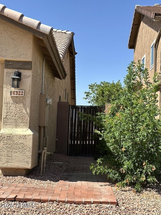 view of side of property featuring stucco siding, a gate, and a tile roof