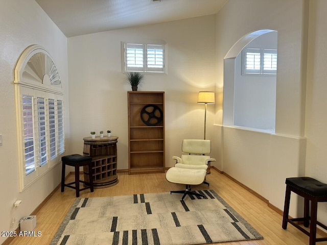living area with arched walkways, wood finished floors, lofted ceiling, and baseboards