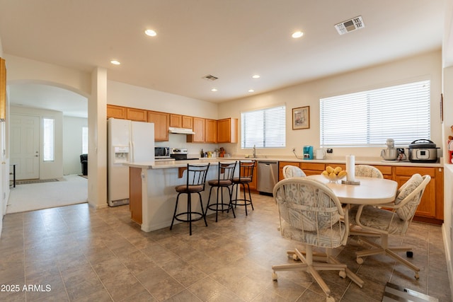 170 E Canary Ct, San Tan Valley, AZ 85143 - kitchen featuring appliances with stainless steel finishes, under cabinet range hood, arched walkways, a center island, and a kitchen breakfast bar