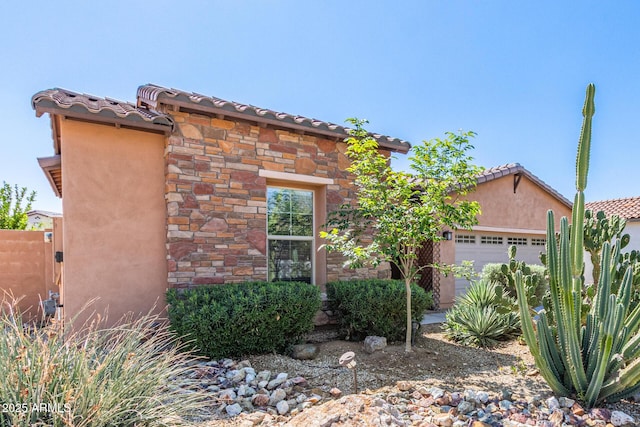 view of front facade with stucco siding, stone siding, a garage, and a tiled roof