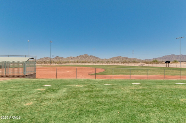 view of tennis court with a lawn, a mountain view, and fence