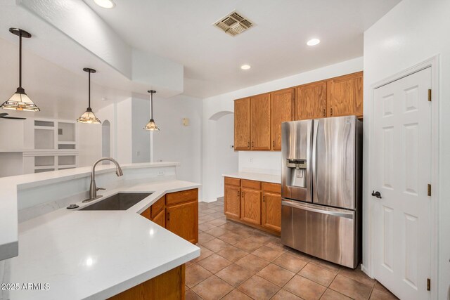 13599 W Monte Vista Rd, Goodyear, AZ 85395 - kitchen with stainless steel fridge with ice dispenser, a sink, arched walkways, brown cabinetry, and hanging light fixtures