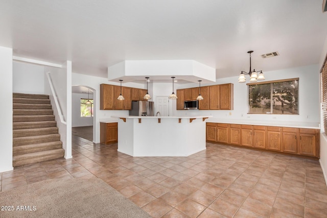 13599 W Monte Vista Rd, Goodyear, AZ 85395 - kitchen with stainless steel appliances, a breakfast bar area, arched walkways, light countertops, and brown cabinets