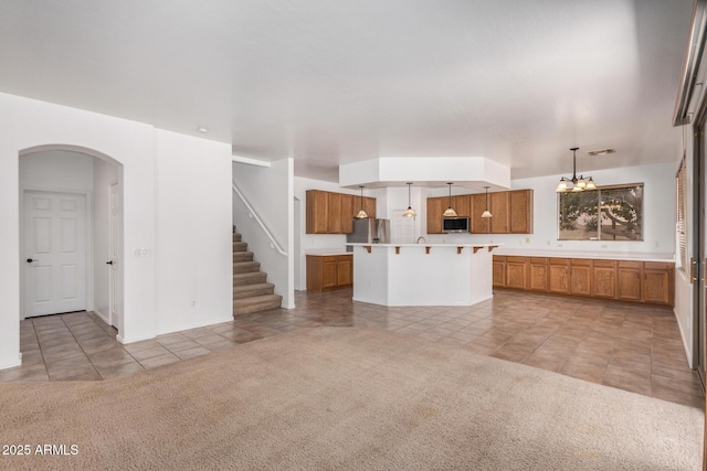 13599 W Monte Vista Rd, Goodyear, AZ 85395 - unfurnished living room with light tile patterned flooring, arched walkways, light carpet, and a chandelier