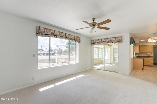 unfurnished living room featuring a sink, baseboards, light carpet, and a ceiling fan