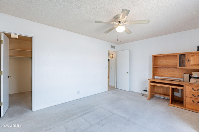 unfurnished bedroom featuring visible vents, a walk in closet, ceiling fan, light colored carpet, and a textured ceiling