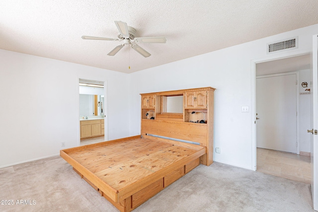 bedroom featuring visible vents, light carpet, ensuite bathroom, a ceiling fan, and a textured ceiling