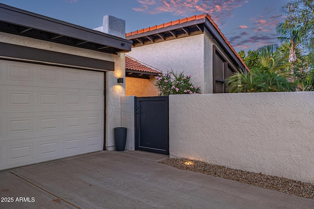 7821 N Via De La Sombre, Scottsdale, AZ 85258 - view of property exterior featuring a gate, stucco siding, a tiled roof, an attached garage, and concrete driveway