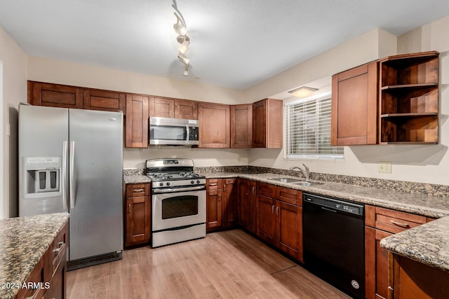 kitchen with appliances with stainless steel finishes, light stone counters, light hardwood / wood-style flooring, and sink