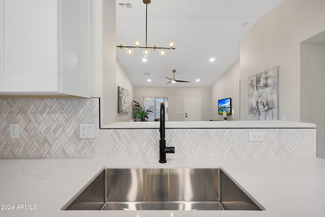 interior details with tasteful backsplash, light stone counters, sink, white cabinetry, and hanging light fixtures