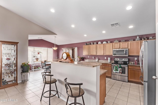 kitchen featuring light tile patterned floors, a breakfast bar, stainless steel appliances, a kitchen island, and decorative light fixtures