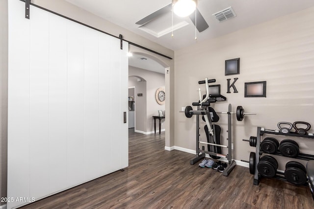 exercise room with dark wood-type flooring, ceiling fan, and a barn door