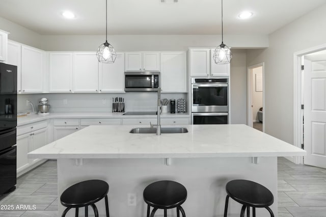 kitchen with a kitchen bar, black appliances, white cabinets, and a sink