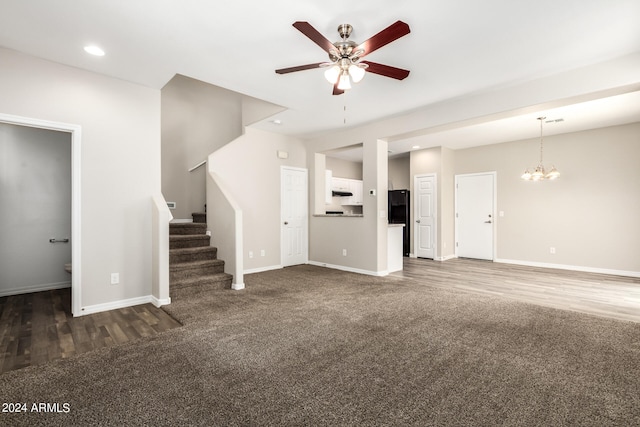 unfurnished living room featuring ceiling fan with notable chandelier and dark hardwood / wood-style floors