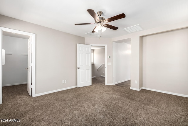 unfurnished bedroom with a walk in closet, dark colored carpet, ceiling fan, and a closet