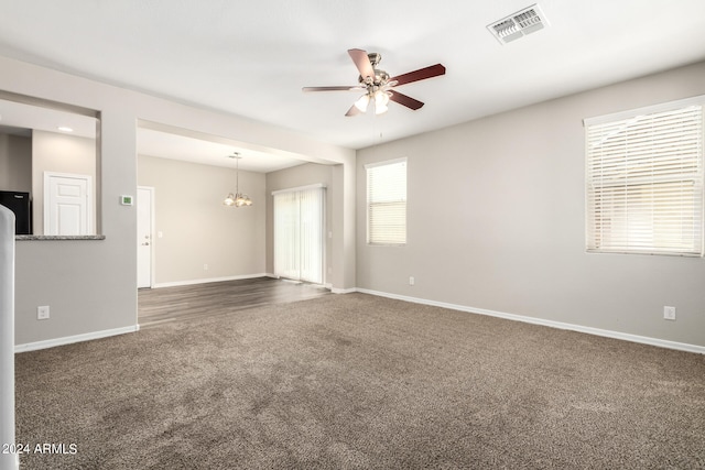 carpeted spare room featuring ceiling fan with notable chandelier