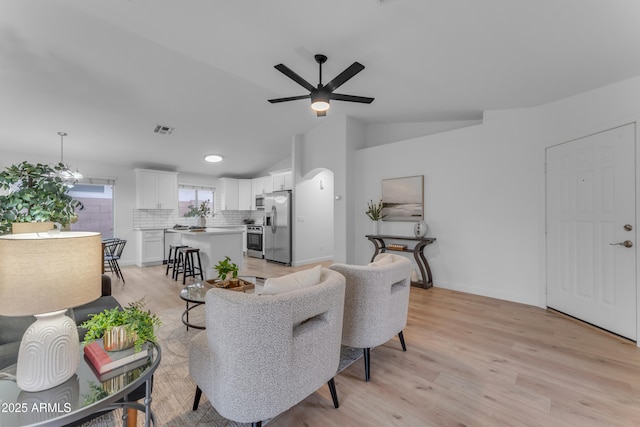 living room featuring arched walkways, lofted ceiling, visible vents, light wood-style floors, and a ceiling fan