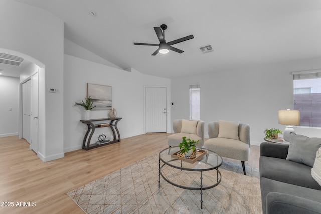 living area featuring lofted ceiling, arched walkways, visible vents, a ceiling fan, and light wood-type flooring