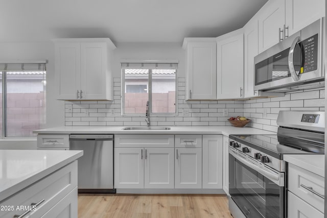 kitchen with tasteful backsplash, appliances with stainless steel finishes, white cabinets, and a sink