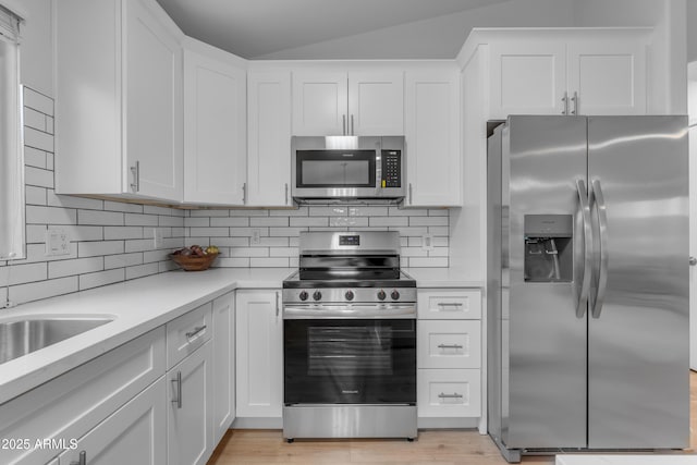 kitchen with stainless steel appliances, white cabinets, light countertops, light wood-type flooring, and backsplash