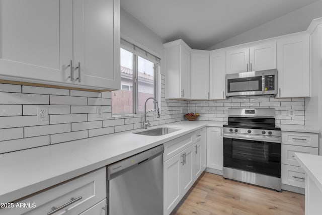 kitchen with lofted ceiling, light countertops, appliances with stainless steel finishes, white cabinetry, and a sink