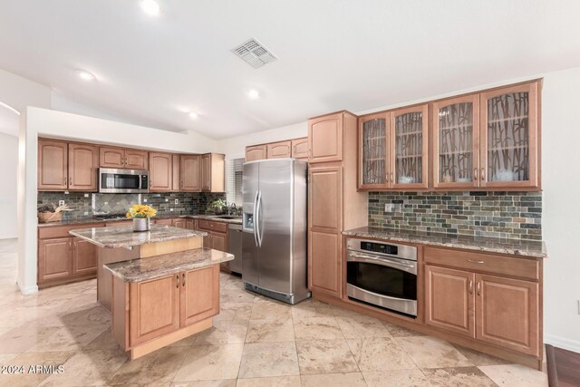 kitchen featuring light stone countertops, tasteful backsplash, lofted ceiling, a kitchen island, and appliances with stainless steel finishes