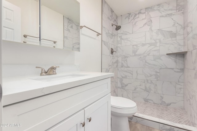 bathroom with hardwood / wood-style flooring, vanity, toilet, and a tile shower