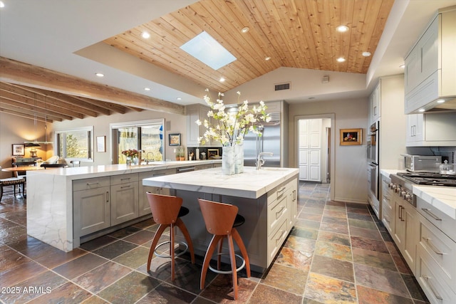 kitchen with a kitchen island with sink, light stone countertops, wood ceiling, and stainless steel appliances