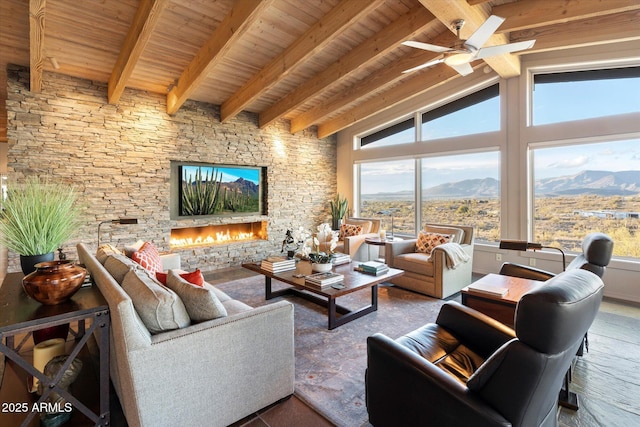 living room with a stone fireplace, vaulted ceiling with beams, ceiling fan, wood ceiling, and a mountain view