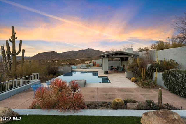 pool at dusk featuring a mountain view, a gazebo, and a patio