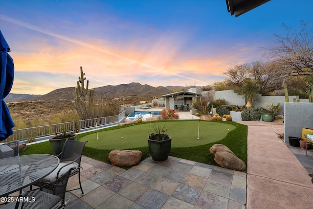 patio terrace at dusk with a mountain view and a fenced in pool