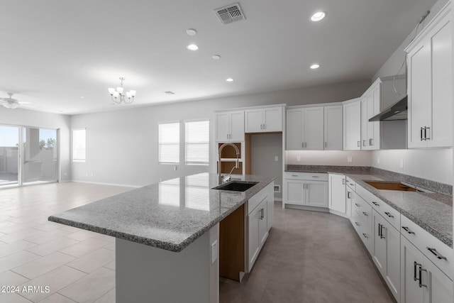 kitchen with a kitchen island with sink, white cabinetry, light tile floors, and ceiling fan with notable chandelier