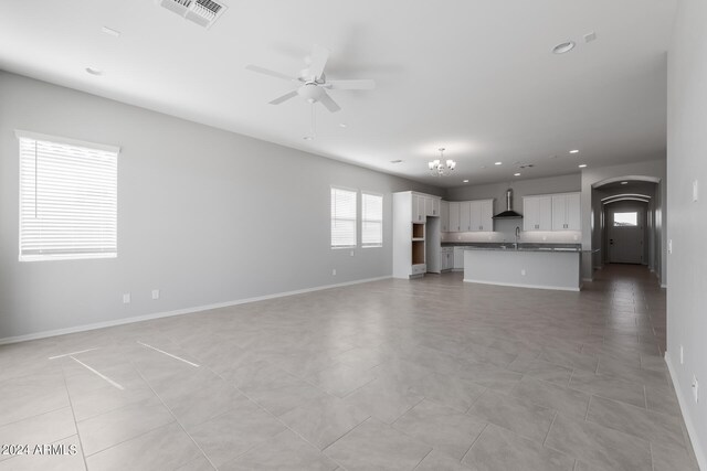 unfurnished living room with sink, a wealth of natural light, light tile floors, and ceiling fan with notable chandelier