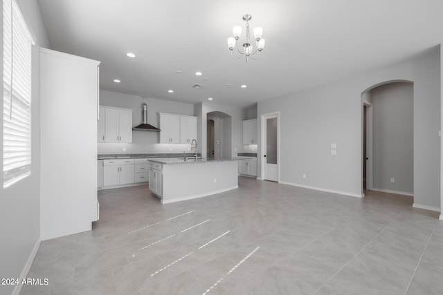 kitchen with an inviting chandelier, wall chimney exhaust hood, a center island with sink, and light tile floors