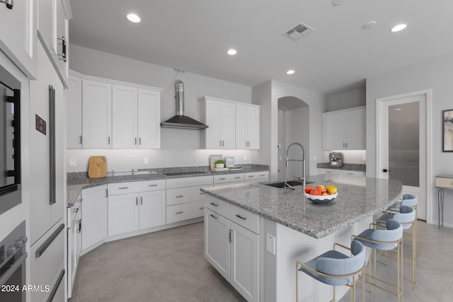 kitchen featuring white cabinets, a kitchen island with sink, and wall chimney exhaust hood