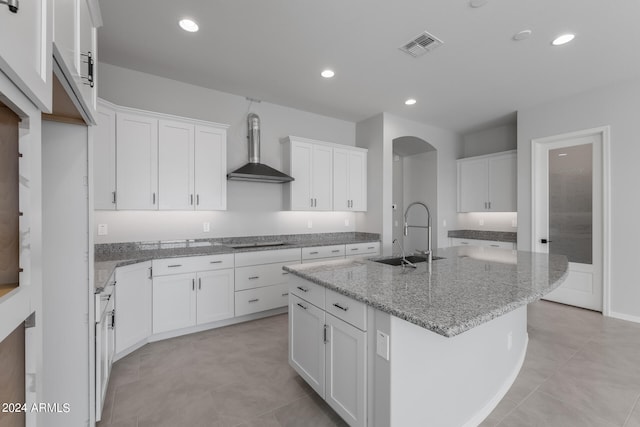 kitchen featuring sink, wall chimney range hood, white cabinetry, and a kitchen island with sink