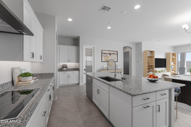 kitchen with light stone counters, white cabinetry, an island with sink, light tile floors, and wall chimney exhaust hood