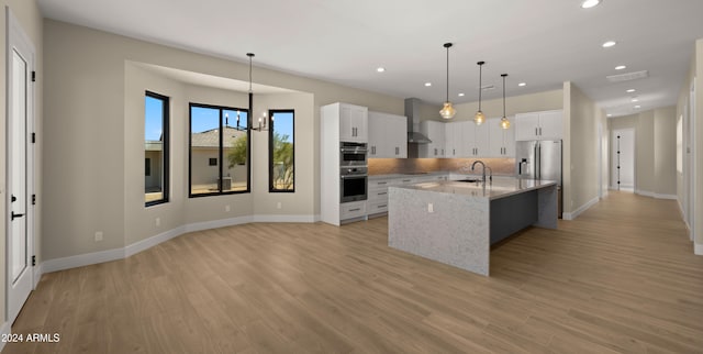 kitchen with pendant lighting, a kitchen island with sink, sink, and white cabinets